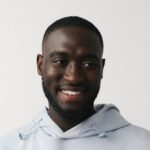 Portrait of a smiling bearded man wearing a light grey hoodie against a white background.